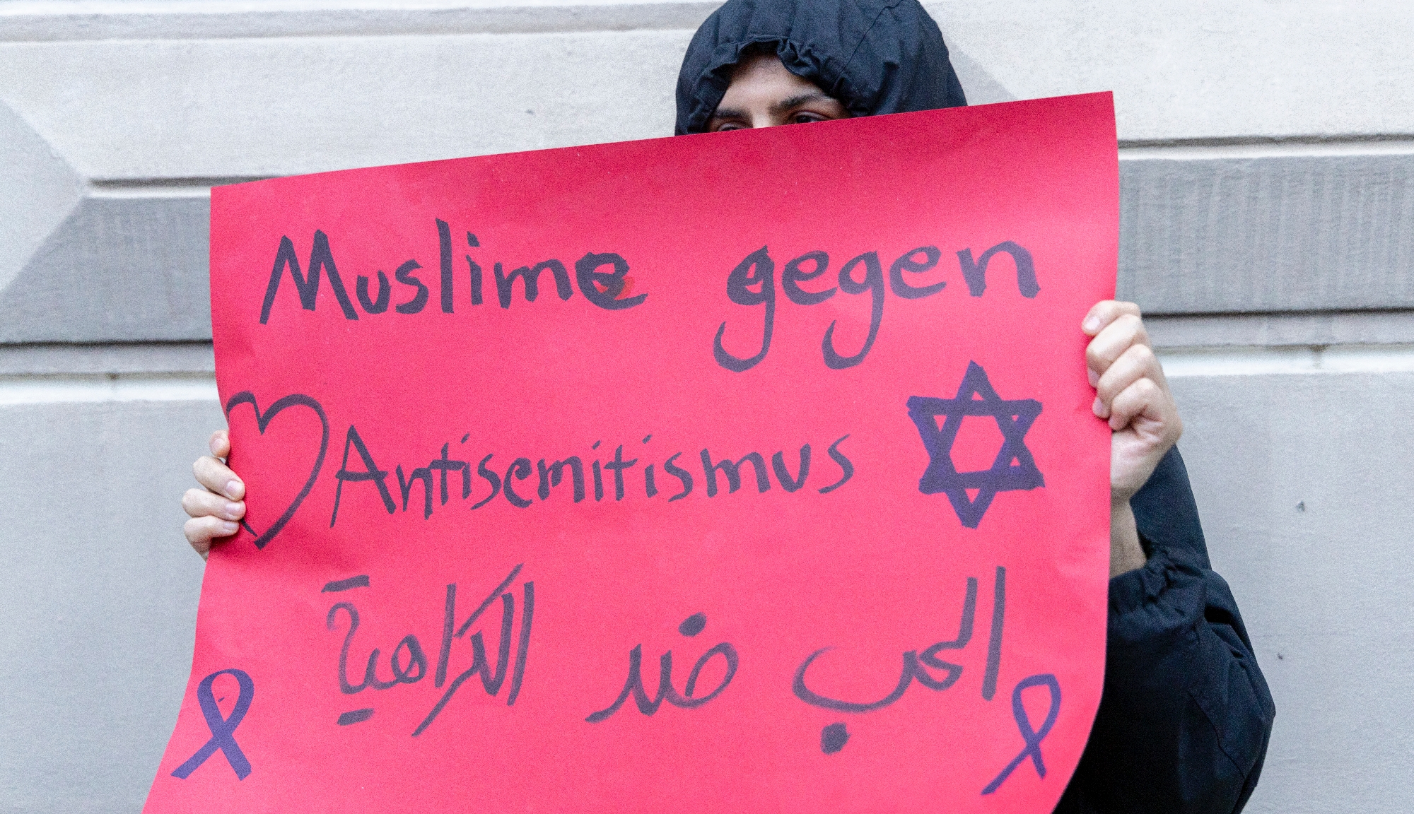Person hält ein Plakat hoch, auf dem steht "Muslime gegen Antisemitismus"