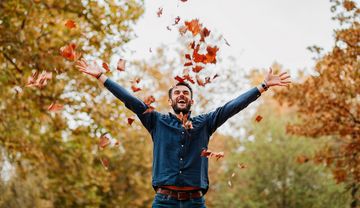 Ein Mann wirft Herbstlaub in die Luft