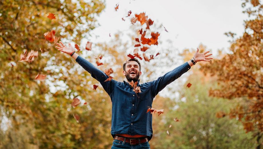 Ein Mann wirft Herbstlaub in die Luft