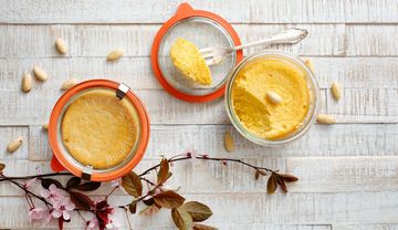 Offene und geschlossene Gläser mit Mandelkuchen, dekoriert mit Mandeln und Blütenzweigen auf hellem Holz