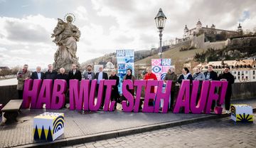 Menschen stehen in Würzburg um das Motto "Hab Mut, steh auf"