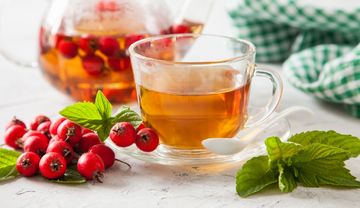 Weißdornbeeren, gefülltes Teeglas, Teekanne und grüne Blätter