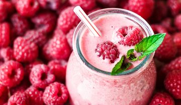 Ein Glas Himbeercreme vor zahlreichen Himbeeren