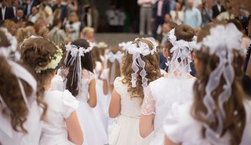 Kommunionskinder stehen im weißen Kleid vor dem Kircheneingang