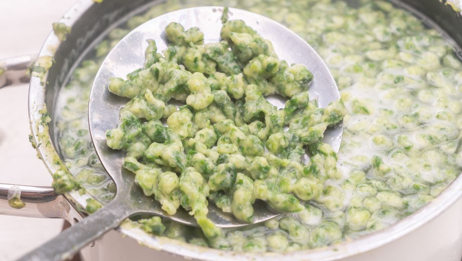 Ein Schöpflöffel hebt Spinatspätzle aus einem vollen Topf