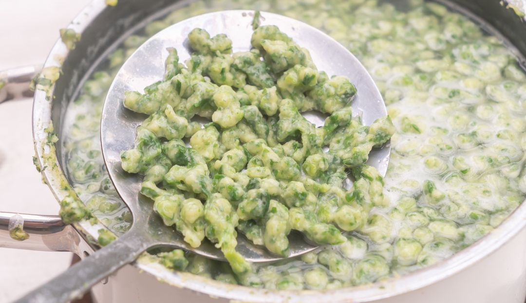 Ein Schöpflöffel hebt Spinatspätzle aus einem vollen Topf