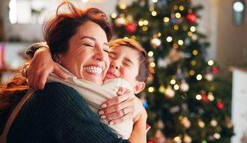 Foto eines Kindes, dass eine Frau freudig vor einem Weihnachtsbaum umarmt
