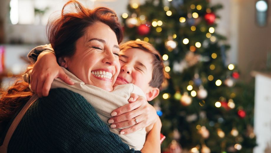 Foto eines Kindes, dass eine Frau freudig vor einem Weihnachtsbaum umarmt