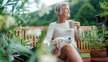 Frau auf einer Bank mit Hund im Grünen und Kaffeetasse neben sich