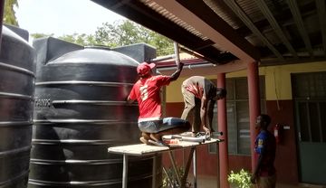 Ein Mann schließt eine Regentonne an die Dachrinne an.