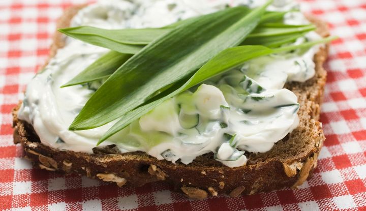 Scheibe K&ouml;rnerbrot mit Quark und B&auml;rlauchbl&auml;ttern auf einem rot-wei&szlig; karierten Tischtuch