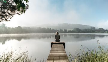 Eine Frau sitzt alleine am Ende eines Steges zu einem See
