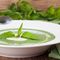weißer Teller mit grüner Suppe, garniert mit Brennnesselblättern, daneben ein Bund Brennnesseln und eine Stoffserviette