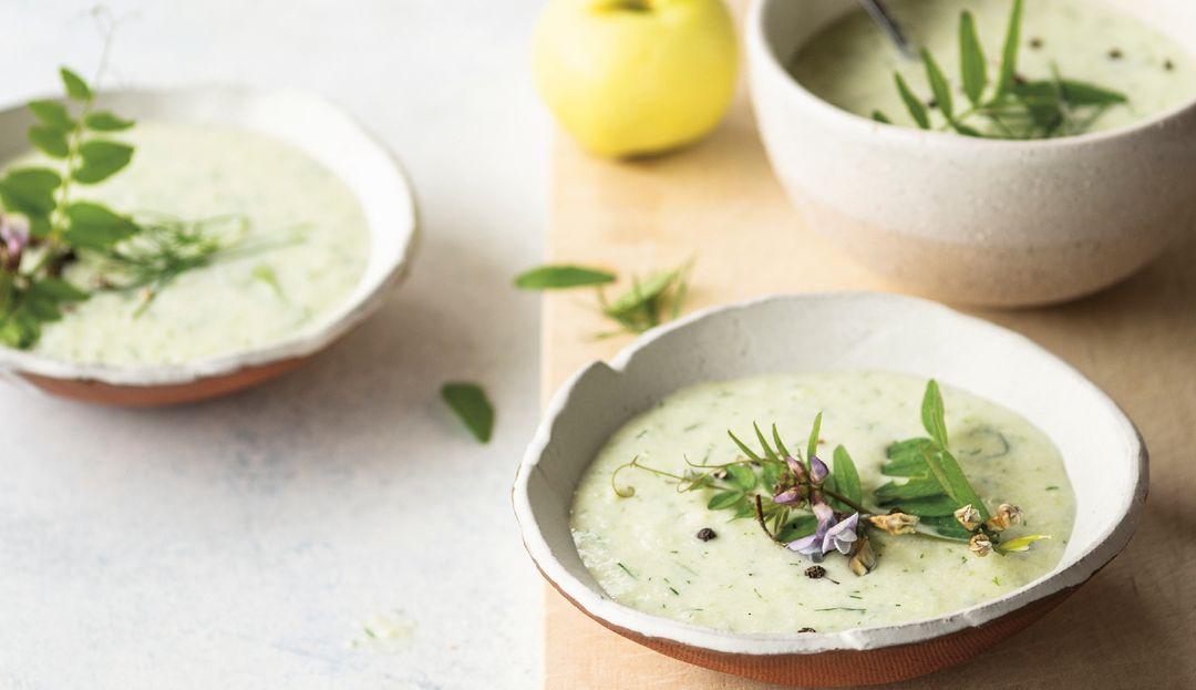 Holzbrett, Löffel und zwei Schalen mit grüner Suppe mit frischen Kräutern dekoriert