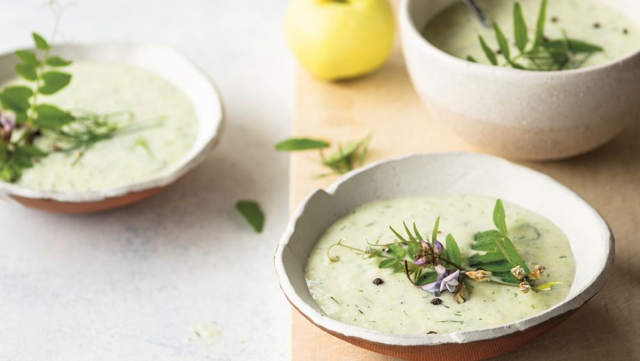 Holzbrett, Löffel und zwei Schalen mit grüner Suppe mit frischen Kräutern dekoriert