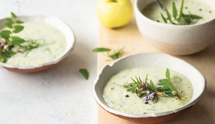 Holzbrett, L&ouml;ffel und zwei Schalen mit gr&uuml;ner Suppe mit frischen Kr&auml;utern dekoriert